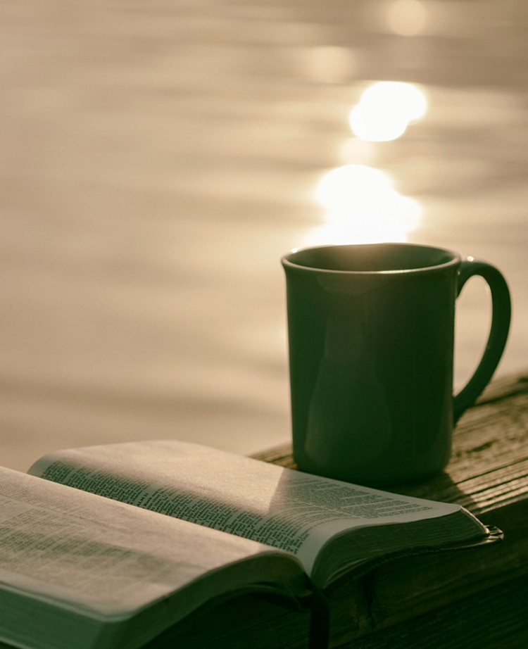 水辺に置かれたコーヒーカップと聖書
